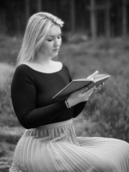 Junge Frau, die auf einer Waldlichtung ein Buch liest.