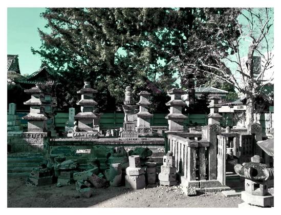 Photo taken at a temple. Behind a fence there were many stone lanterns and mini stone pagodas. I cannot tell if this is spare parts, a mason's workshop, or a spiritual place slightly in decay. I've adjusted the colors and given the shot a greenish hue to everything.