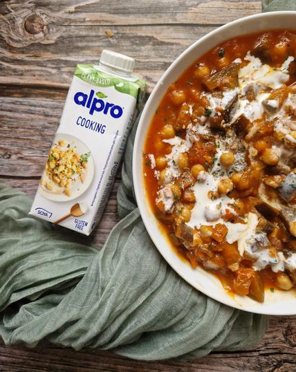 Piatto di stufato di ceci, melanzane e zucca, con sopra la panna da cucina Alpro.
Accanto la confezione del prodotto.