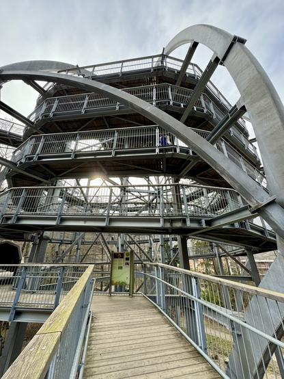 Eine Außenspindeltreppe mit mehreren Ebenen, Holzstegen und Metallgeländern vor einem Hintergrund kahler Bäume und eines klaren Himmels.