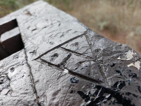 a symbol etched into a wooden railing: a pyramid divided into three segments by a T in the middle, with a dot inside each segment