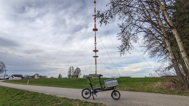 Ein Yoonit Cargobike auf einer Strasse stehend, im Hintergrund der mit Stahlseilen verspannte Hebertsfeldener Sendemast