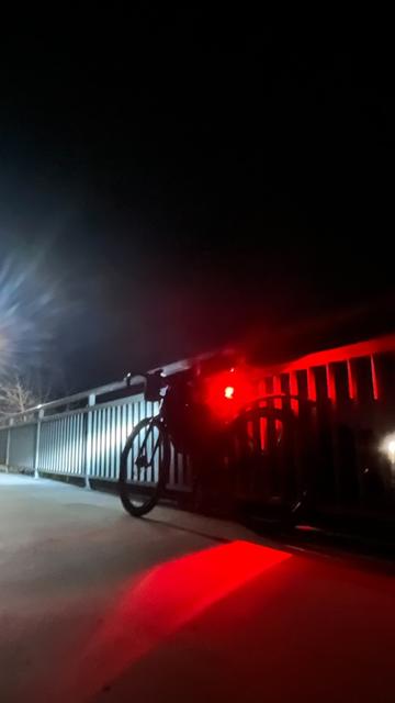 Dunkles Fahrrad in dunkler Nacht auf einer Brücke am Geländer