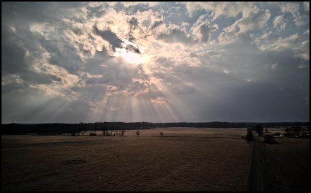 Aerial view of some brown fields. Focus of photo is sunlight breaking through the clouds and a fan of sun rays spreaking in all directions.