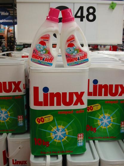 ein grosses waschmittelpaket "linux" mit zwei weichspuelerflaschen drueber, mit dem namen "micro&soft"