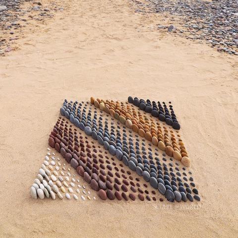 A square made out of different coloured rocks from the seashore. They have been arranged diagonally according to size.