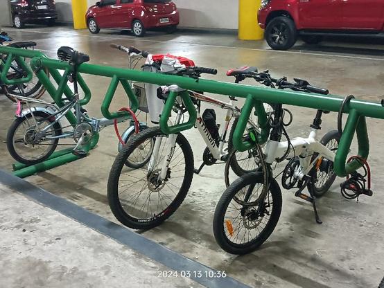 Photo of a bicycle rack at the basement parking of a mall. Parked are a very old blue 16" Japan surplus foldie, a white mountain bike, and a white Himo Z20 ebike. The ebike is secured with 3 locks.