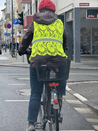 Cyclist as seen from behind, wearing normal clothes but a flourescent yellow high visibility jacket that's made from lace.