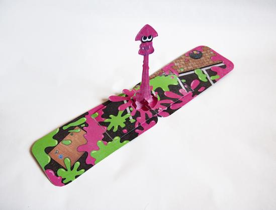 Foto de mi tarjeta de Splatoon, con un calamar haciendo un supersalto sobre un campo de batalla manchado de verde y magenta.