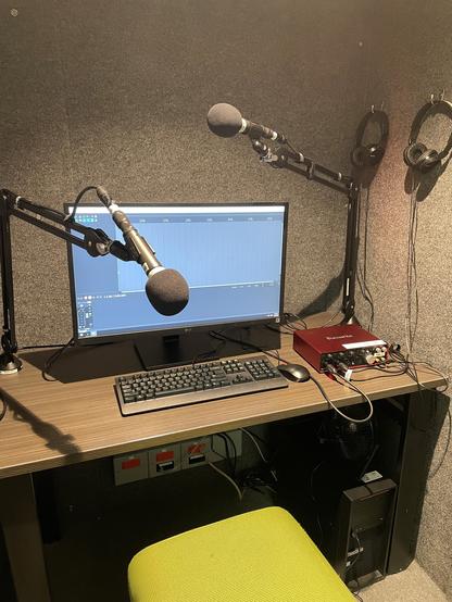 Photo taken inside one of the sound booths in the Inspiration Lab showing REAPER software open on a nice big monitor, a couple of mics, a Focusrite audio interface, and some headphones hanging from hooks on the wall.