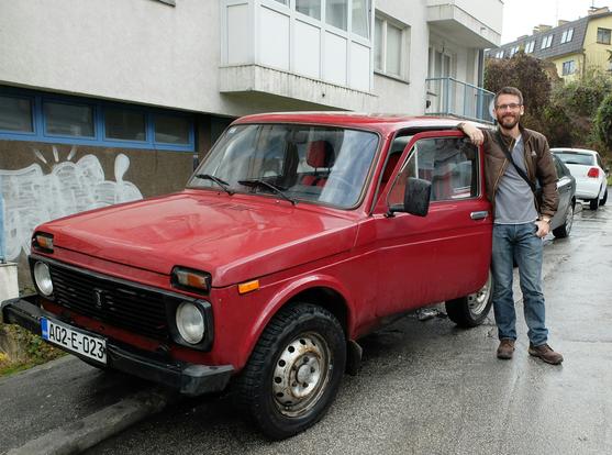 A younger version of me at the open door of my red Lada niva on a Sarajevo street