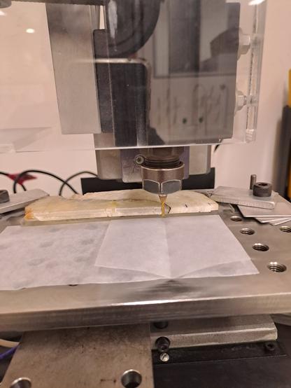 A slab of speleothem mounted on a CNC mill bench. You can see the colour of the material changes dramatically about 2/3 through the sample.