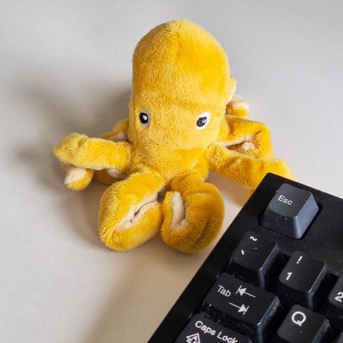 Pequeño pulpo amarillo de peluche junto a un teclado de ordenador.