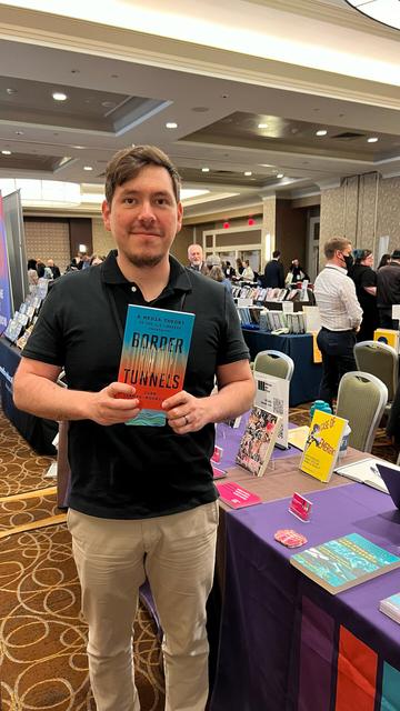 Juan Llamas-Rodriguez at the Ideas on Fire conference booth holding his book