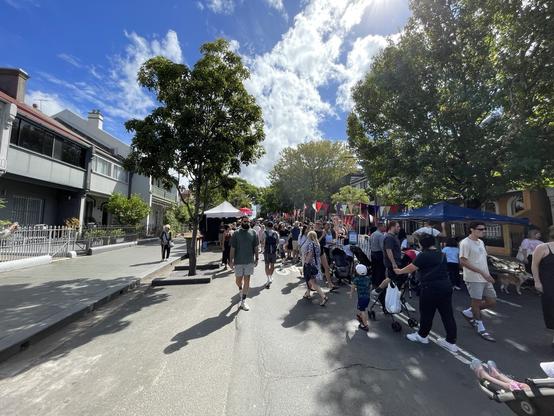 A sunny street festival with people walking and visiting stalls.