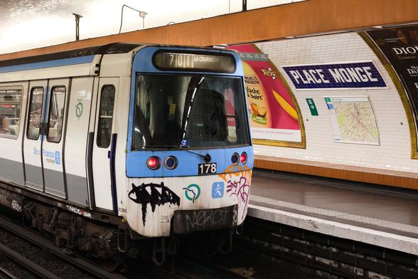 Une rame de métro de Paris à l’arrêt, à la station Place Monge. C’est un autre angle, plus rapproché sur la cabine du conducteur en queue de rame, mais une partie du quai et le nom de la station sont visibles.