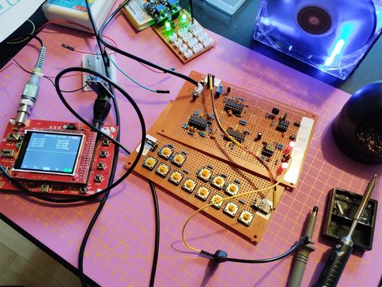 the board is lying on the table with power and key board connected and switches on. the trigger and gate LEDs are constantly on. next to it is an oscilloscope with the probe's ground reference connected to one of the pins. I'm trying to spot the error in the output buffer of trigger and gate