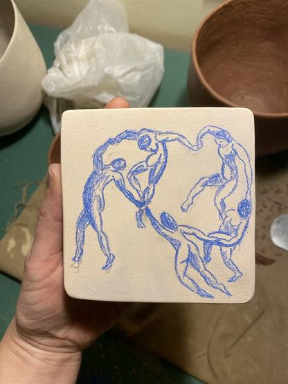 a photo of my hand holding a bisqued ceramic box showing its lid. The lid has a drawing made with blue oxide pencil that looks pretty much like a colored pencil sketch. The drawing represents the dancers from Matisse’s painting called The Dance from 1910. This box is in fact for watercolors. Inside it has four little square boxes for holding watercolor, ideally blue, red, yellow and black.