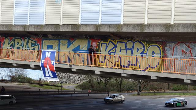 Alphornbläser (kaum zu erkennen) auf dem Radweg unterhalb der Autobahn auf der Europabrücke über den Main. Am Geländer hängt ein großes Banner mit unserem Logo.