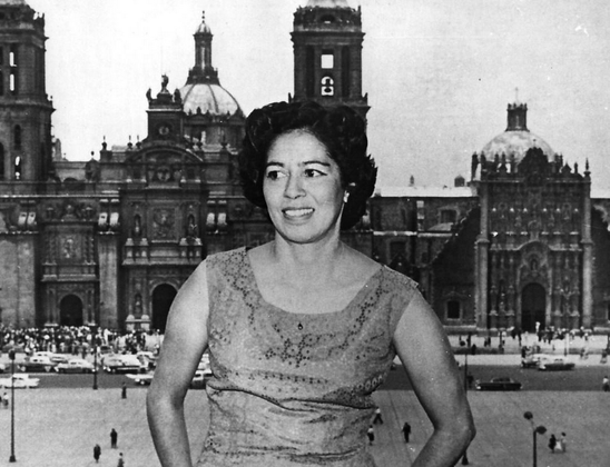 Ángela Alessio Robles in undated black and white photo, leaning against an unshown edge, with historical city scape in background.