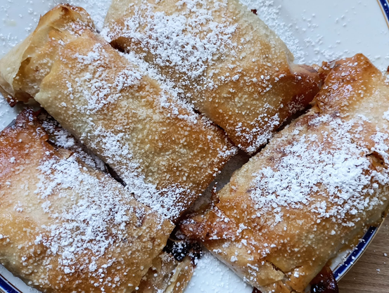 Auf einem Teller 4 kleine fertig gebackene Apfelstrudel - mit Puderzucker bestreut