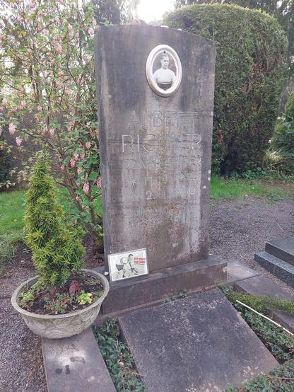 Foto vom Albert Richters Grab (bevor ich  die Blumen und Kerze hingestellt habe).  Ein schlichtes Einzelgrab mit einem dauerhaft befestigtem Portraitfoto von ihm im Radtrikot. Der Grabstein besteht aus Beton, die Gravur lautet: Albert Richter Rennfahrer *14.10.1912 +2.1.1940 „Wer dich gekannt / vergisst dich nie“.
An den Grabstein lehnt eine Postkarte von Albert Richter auf dem Rennrad mit der Aufschrift "With respects from Canada":  Auf dem Grabstein liegen einige kleine Kieselsteine. Links vor dem Grabstein steht ein kleines Bäumchen in einer grauen Schale. Sonst ist kein "Schmuck" auf dem Grab.