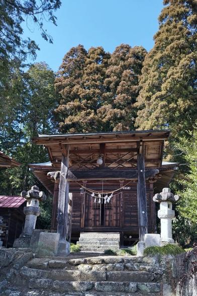 A small weathered wooden shrine on the side of a hill surrounded by woods. A crooked stone staircase leads up to its location. This picture was taken from ground level.