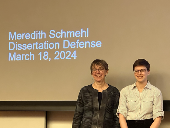 Photo of Meredith Schmehl and advisor Jennifer Groh posing in front of a screen showing a PowerPoint slide.