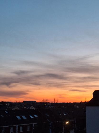 Sunset in light blue fading towards orange. Dark house silhouettes in the front.
