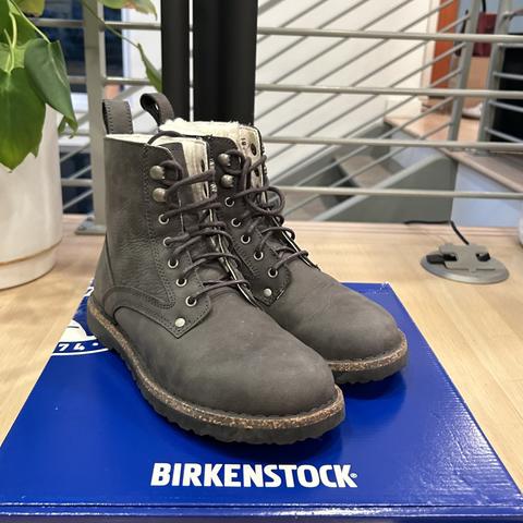 Gray Birkenstock combat boots with white fleece lining on top of blue Birkenstock box.