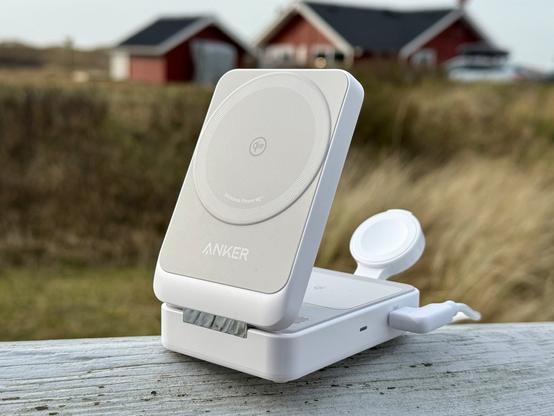 Anker MagGo Qi2 3-in-1 Ladestation in Weiß auf einem Zaun, im Hintergrund Dünen und ein rotes Ferienhaus.