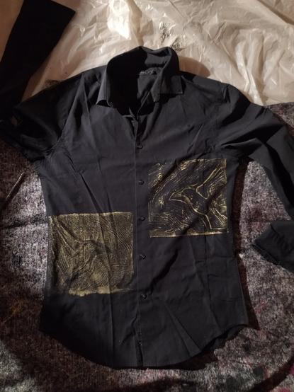a picture of a black shirt with two linocut print of a bird facing each other, wings extented, in golden paint.