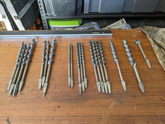 Several restored brace bits ready for use. They are lying on a timber workshop bench.