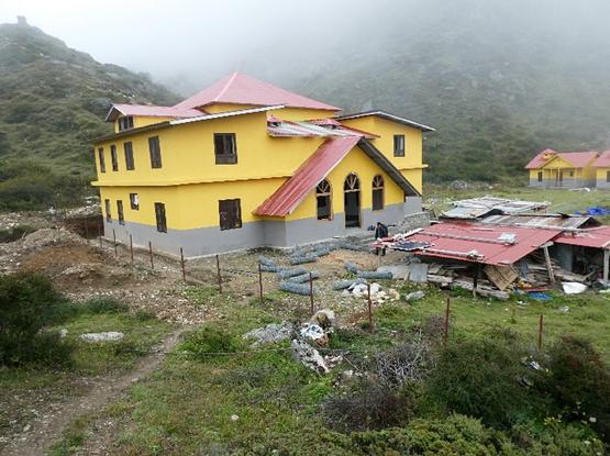 Bright yellow and gray multistory buildings with peaked red roofs are under construction near Kampuchen Nepal on a foggy day. They are part of the Snow Leopard Research Center and its living quarters