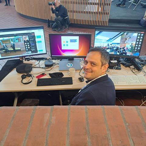 Technik Chef Sebastian grinst in die Kamera und auf dem Tisch sieht man 2 Kamera beim stream und die Teilnehmer als icon