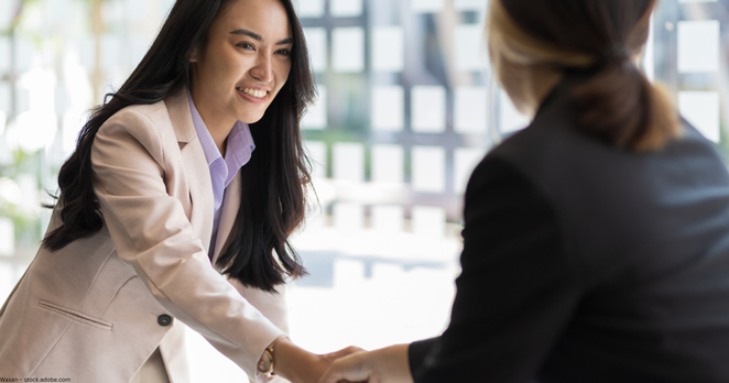 Two women shaking hands smiling.