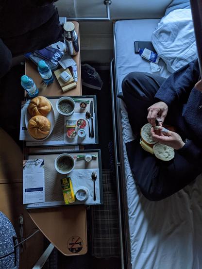 Blick vom oberen Stockbett im Nachtzug auf das untere Bett mit Frühstückstisch davor inkl. Brötchen und Kaffee
