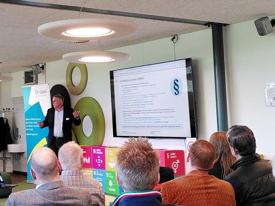 A man presenting to a small audience in front of a screen and Sustainable Development Goals