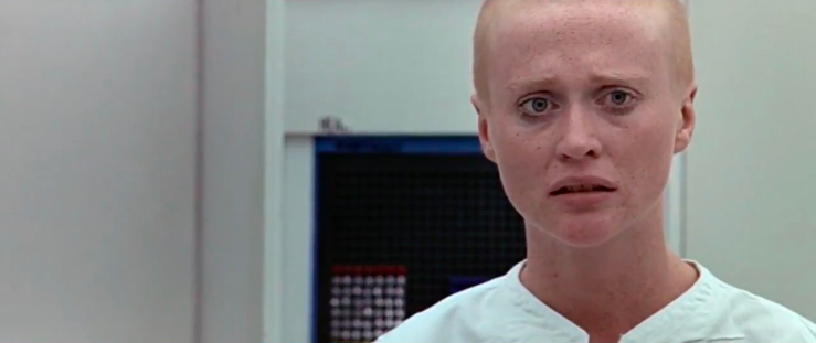 Scenes from a futuristic sci fi movie. A bald woman looks upset about something.