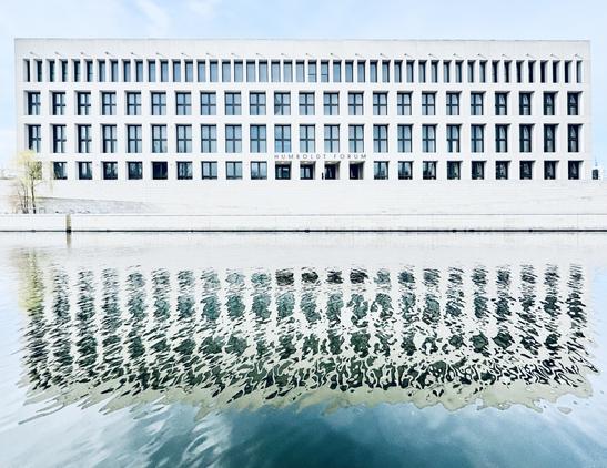 Modern building with large windows and the inscription "Humboldt Forum" reflected on a body of water.