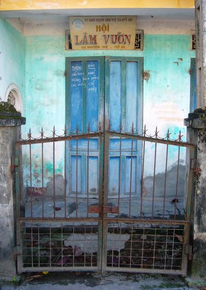 Painted sign mounted above a double door set within walls of turquoise. This all sits behind a metal gate in a scene of graceful decay.