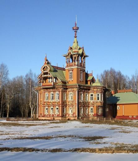 A big wooden house with a fancy tower, carefully restored to its original form. The sky is blue, and there's snow on the ground.