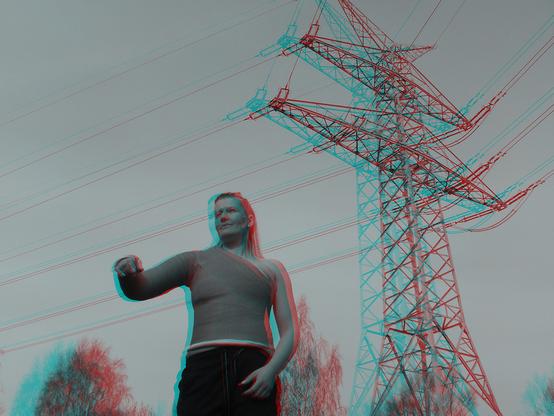 Anaglyphes 3D Bild einer Frau, die mit einem Schultergips vor einem Hochspannungsmast steht.