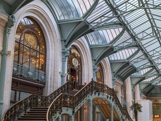 View of the front door of a restaurant, on the first floor following a flight of stairs. The facade of the restaurant is overhanged with an art-deco-style steel and glass ceiling.