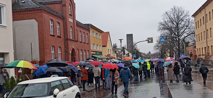 Blick auf die Dorfschule, davor die Ansammlung der Demonstranten, fast alle mit Regenschirm