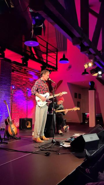 Zwei Musiker mit E-Gitarre und Bass auf der Bühne eines kleinen Saals. Rote Beleuchtung.