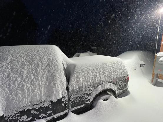 Deep snow covering a truck and car at night under artificial LED lighting.