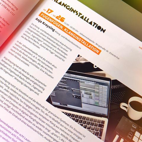 page inside the catalogue, announcing soundinstallation "fugenfuegen" of Anja Kreysing. White paper, header bold black & orange typo, text in black typo, photo of Mac book with Ableton live, accordion, novation launch key 3 controller keyboard and a white cup with black coffee :-D