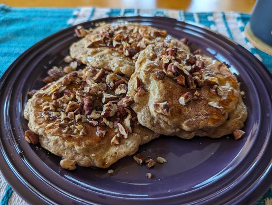 three pancakes topped with pecans and maple syrup, on a purple plate
