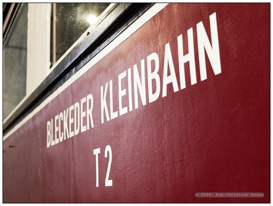 Aufschrift "Bleckeder Kleinbahn" in cremefarbener, serifenloser Schrift auf der weinrot lackierten Seitenwand eines historischen Schienenbusses aus den 1930er-Jahren.